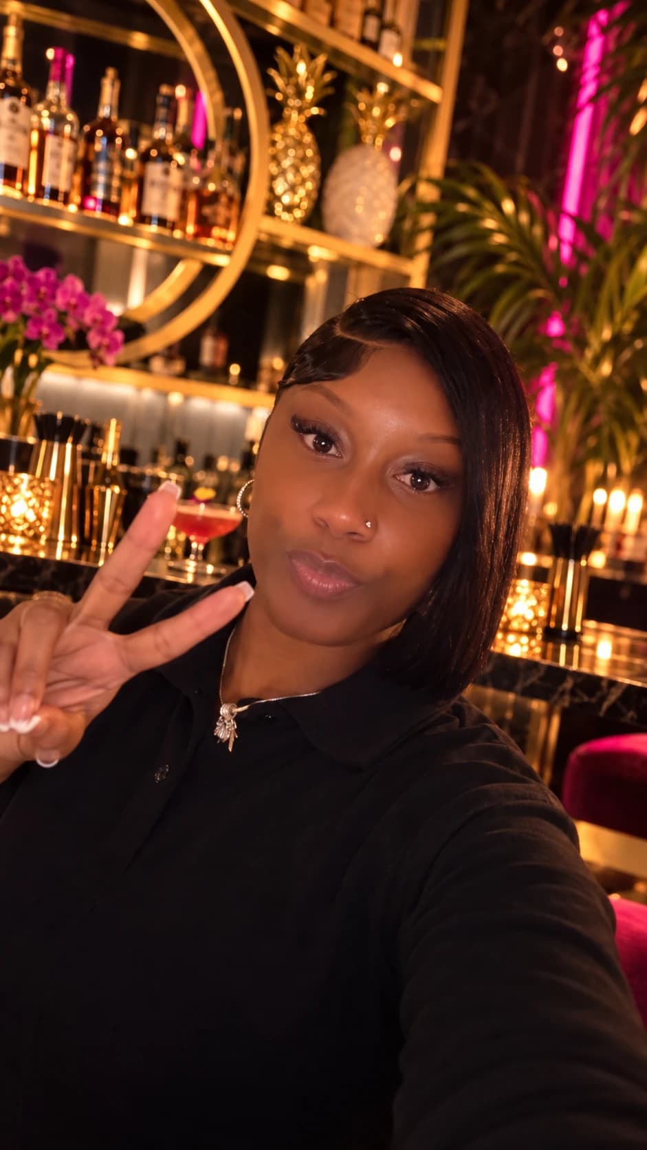 BigCee posing with a peace sign at a gold and pink bar