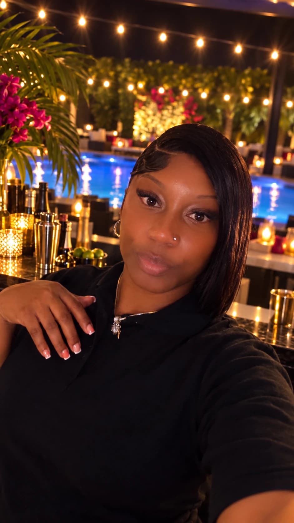 BigCee beside a poolside bar under warm string lights